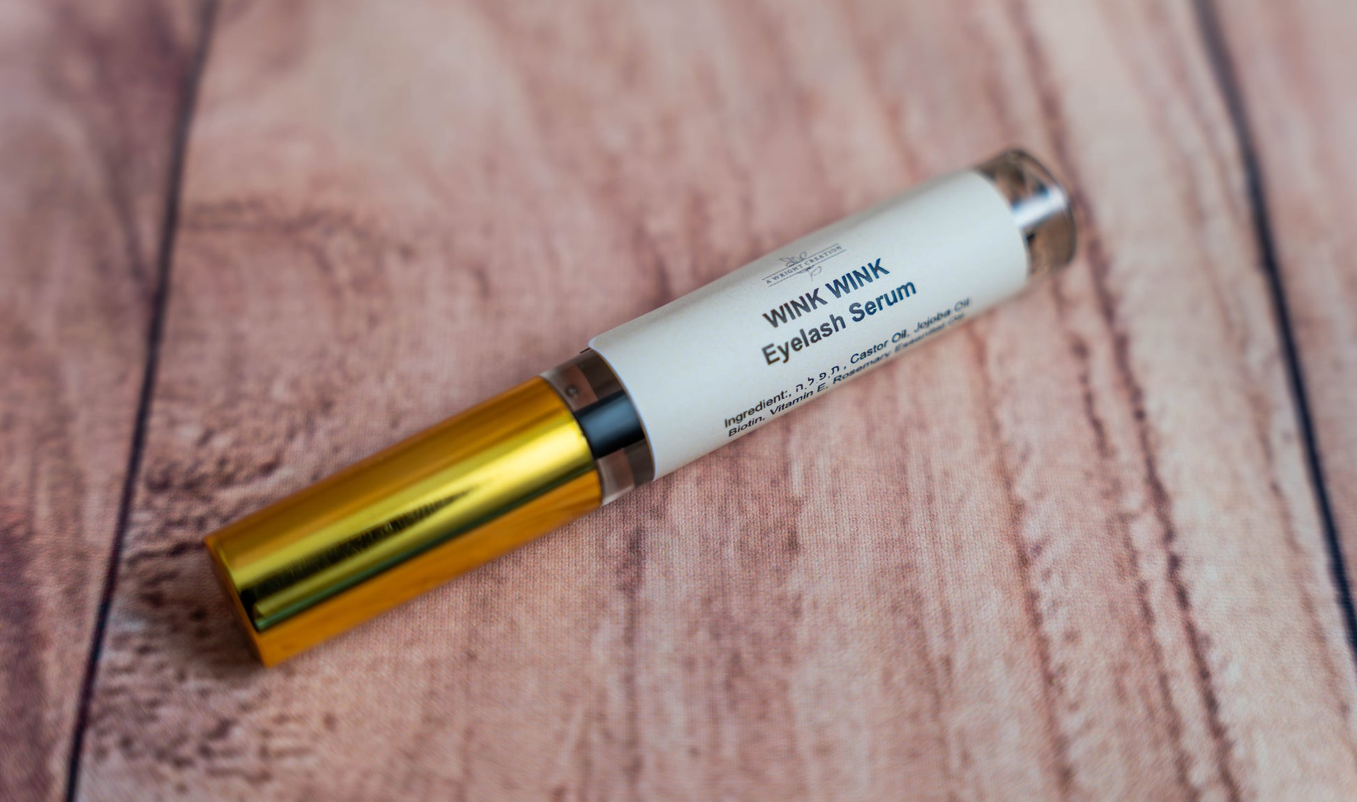 A Wright Creation Wink Wink Eyelash Serum in sleek gold and white packaging, formulated with natural ingredients like castor oil, jojoba oil, and biotin to promote stronger, healthier lashes, ideal for sensitive skin and eco-conscious beauty routines.